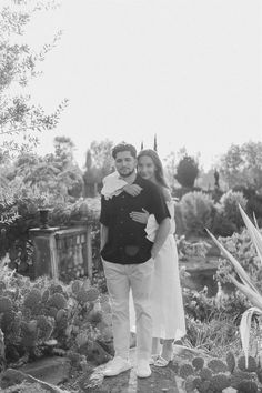 a man and woman standing next to each other in front of some plants on the ground