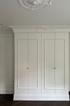 an empty room with white cupboards and wood flooring on the walls, in front of a chandelier