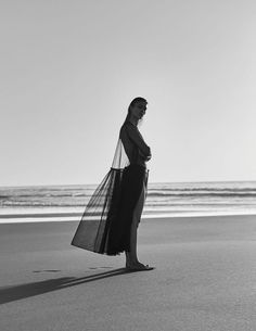 a woman is standing on the beach with her back to the camera, wearing a long black dress