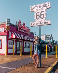 a woman standing on the side of a road next to a sign that says santa monica 66