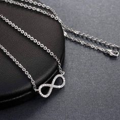 Centered between the two lengths of shiny silver tone chain, this miniature eternity symbol appears to float along the neck. Completely encrusted in micro CZ stones creating incredible shimmer. At only 2 cm this is truly subtle and graceful. This necklace is perfect for women, teens or young children. Length: 18 inch chain Stones: CZ Metal: Sterling Silver, 3 layers of platinum plating. Comes in a gift box. (Reg $45.99) White Gold Infinity Jewelry With Cubic Zirconia, White Gold Infinity Necklace With Cubic Zirconia, White Gold Infinity Cubic Zirconia Jewelry, Silver Infinity Clavicle Chain Jewelry, Silver Infinity Clavicle Chain Necklace, Silver Infinity Jewelry With Adjustable Chain, Silver Infinity Jewelry, Silver Infinity Necklace In Dainty Style, Silver Infinity Metal Necklace