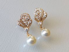 two pairs of pearl and diamond earrings on a white surface with light colored fabric in the background