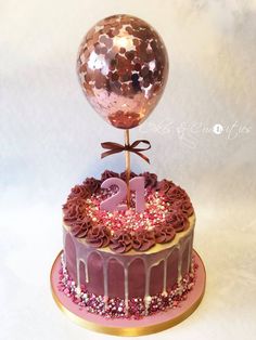 a birthday cake decorated with pink and gold icing, topped with a large balloon