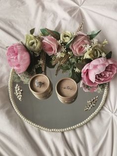 two wedding rings are placed in front of pink flowers on a white sheet with pearls