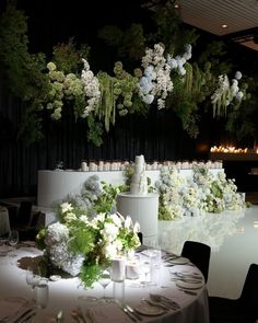 the table is set with white flowers and greenery hanging from the ceiling above it