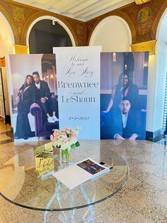 a glass table topped with a vase filled with flowers and two large posters behind it