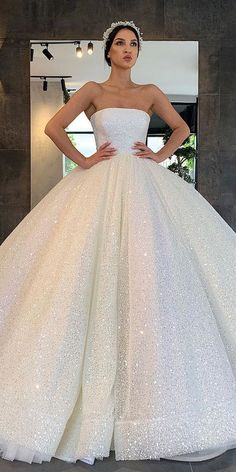 a woman in a white wedding dress standing next to a mirror with her hands on her hips