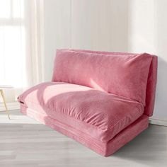 a pink couch sitting on top of a hard wood floor next to a white wall