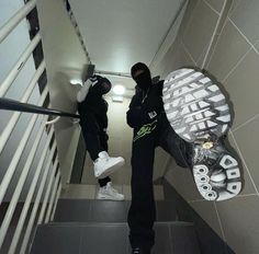 two men in black jackets and white sneakers are standing on the stairs with their skateboards