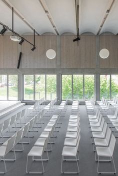 rows of white chairs in an empty room with large windows on the wall and floor