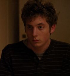 a young man with curly hair wearing a striped shirt and looking at the camera while sitting down