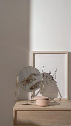 a mirror sitting on top of a wooden table next to a vase and framed artwork