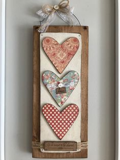 three hearts are hanging on the wall in a wooden frame with ribbon and bow attached to it