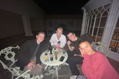 a group of people sitting around a table with drinks on it and one person taking a selfie