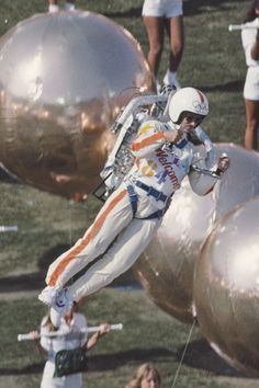 a man in white and orange jumps over some large gold balloons while people watch from the sidelines