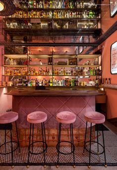 three pink stools in front of a bar with bottles on the wall and shelves