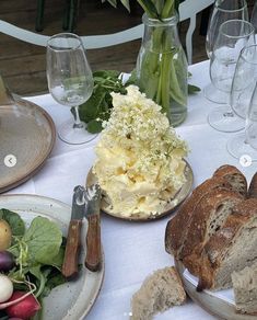 a table topped with bread and vegetables next to wine glasses on top of a white table cloth