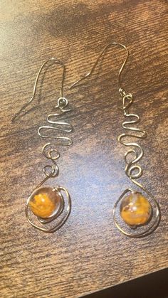 two yellow glass beads are hanging from silver wire earrings on a wooden table with a wood surface