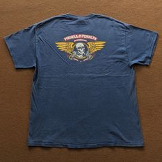 a blue t - shirt with a skull and wings on the front, sitting on a brown surface