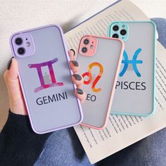 two cell phones with zodiac signs on them are held up in front of an open book