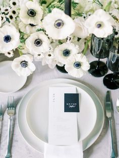 the table is set with white flowers and black place settings for an elegant dinner party