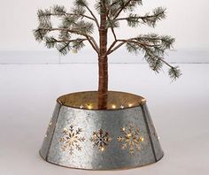 a small tree in a metal pot with snowflakes on the rim and lights around it