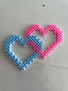 a heart made out of beads sitting on top of a white table next to a blue and pink object