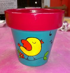 a blue cup with a yellow bird painted on it's side sitting on a pink table