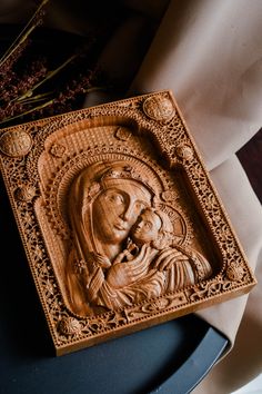 an intricately carved wooden plaque depicting the virgin mary and child jesus, on a table