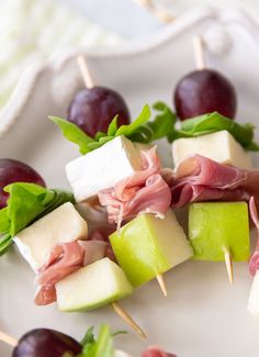 several appetizers are arranged on skewers with grapes and cheese