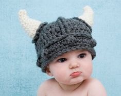 a baby wearing a crocheted hat with horns on it's head, sitting in front of a blue background