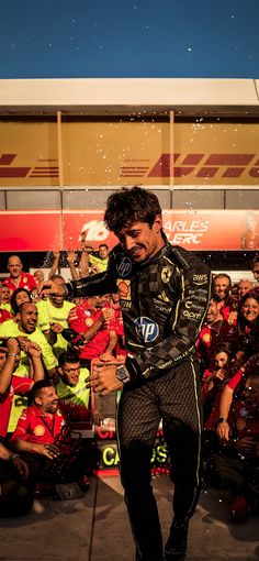 a man is walking in front of a crowd with his hand on his hip while wearing a racing suit