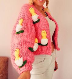 a woman wearing a pink knitted sweater with ducks on the front and sides, while standing next to a wall