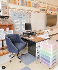 a desk with a chair, computer monitor and printer on it in front of a chalkboard