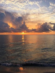 the sun is setting over the ocean with clouds in the sky and water on the beach