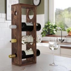 a wooden wine rack with several bottles and two glasses on the counter top next to a clock