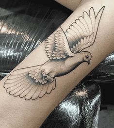 a black and white photo of a dove tattoo on the leg, with wings spread out