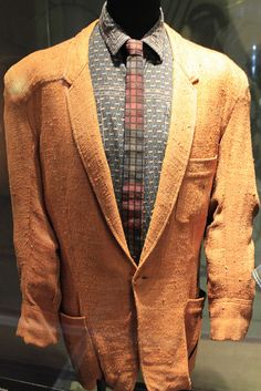 an orange jacket and tie on display in a glass case with a black mannequin's head