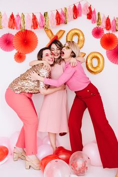 three women hugging each other in front of balloons and streamers