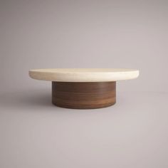 a round table with a wooden base and white marble top on a grey background in front of a gray wall