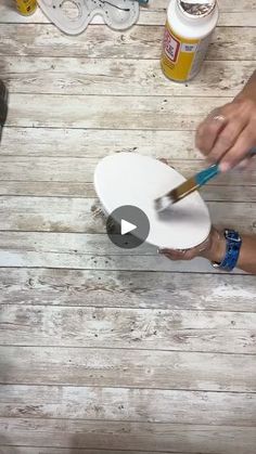 two people using paintbrushes on a white plate with wood planks in the background