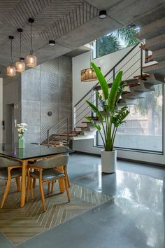 a dining room table with chairs and a potted plant in front of the stairs