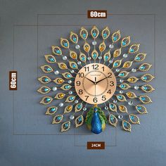 a gold clock with blue and green feathers on it's face is shown in front of a gray wall