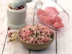 a wooden bowl filled with chopped meat next to a salt shaker and pepper grinder