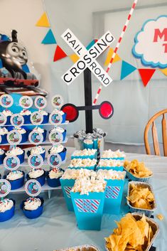 a table topped with lots of food and cupcakes next to a train sign