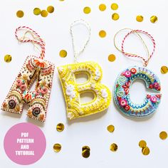 three letters made out of fabric and beads on a white surface with gold confetti