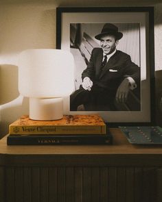 a lamp sitting on top of a wooden table next to a framed photo and books