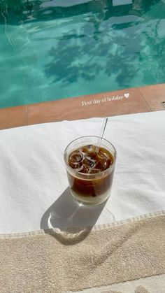 a drink sitting on top of a towel next to a swimming pool