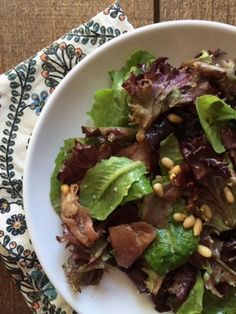 a white bowl filled with lettuce and meat on top of a wooden table