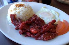 a white plate topped with rice and meat next to an egg on top of it